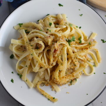 Manchego Mac and Cheese with Bacon on a plate. It has a creamy and cheesy sauce with a touch of smokiness from the bacon, coats each piece of pasta. On top, crispy crunchy, indulgent bacon fat cracker crumbs!