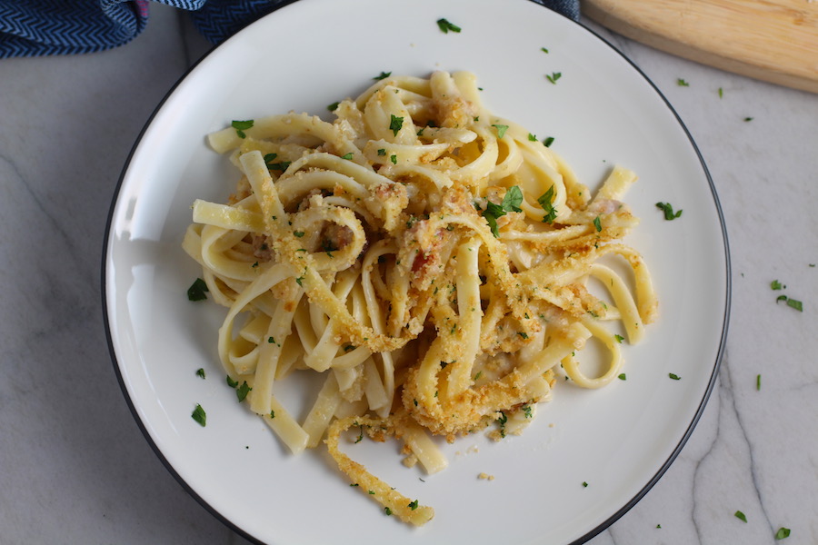 Bacon Mac and Cheese on a plate. It has a creamy and cheesy sauce with a touch of smokiness from the bacon, coats each piece of pasta. On top, crispy crunchy, indulgent bacon fat cracker crumbs!
