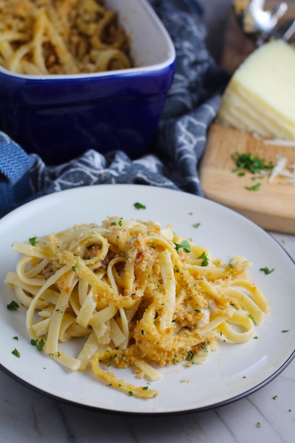 Bacon Mac and Cheese on a plate. It has a creamy and cheesy sauce with a touch of smokiness from the bacon, coats each piece of pasta. On top, crispy crunchy, indulgent bacon fat cracker crumbs!