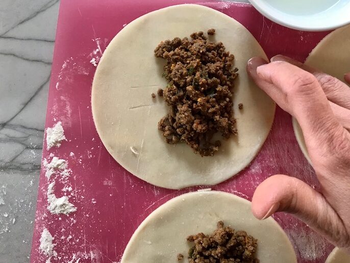 Brushing egg around dough with finger for Ground Beef Empanada closed. Flaky, buttery pastry on the outside with a savory, smokey, salty ground beef filling.