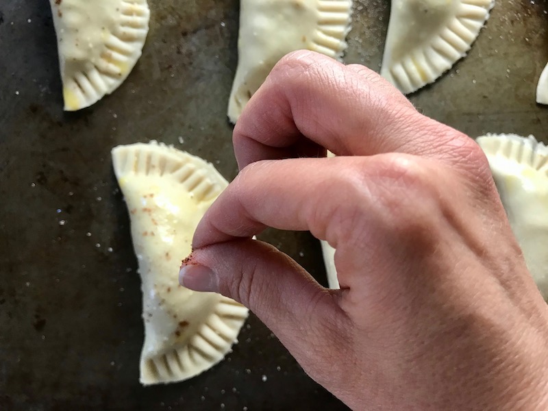 Hand sprinkling chili powder on Ground Beef Empanada. Flaky, buttery pastry on the outside with a savory, smokey, salty ground beef filling.