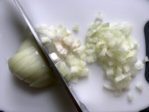 Knife dicing onion for Shell Pasta with Italian Sausage and Kale. It's loaded with a salty homemade Chicken Italian Sausage flavored with garlic and fennel in a parmesan, garlic and kale sauce.