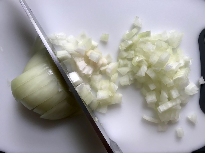 Knife dicing onion for Shell Pasta with Italian Sausage and Kale. It's loaded with a salty homemade Chicken Italian Sausage flavored with garlic and fennel in a parmesan, garlic and kale sauce.
