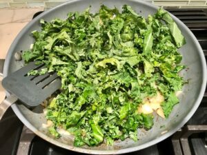 Cooking kale in pan for Shell Pasta with Italian Sausage and Kale. It's loaded with a salty homemade Chicken Italian Sausage flavored with garlic and fennel in a parmesan, garlic and kale sauce.