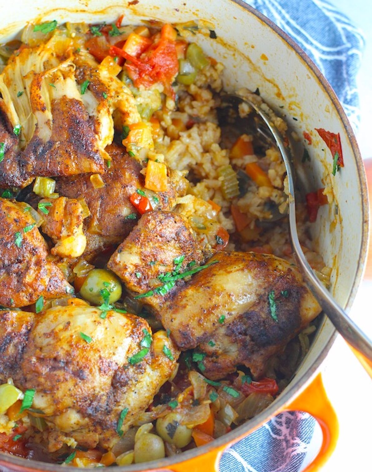Spanish Chicken and Rice with olives and veggies in a pot with spoon. It's hearty, smokey, and delicious!