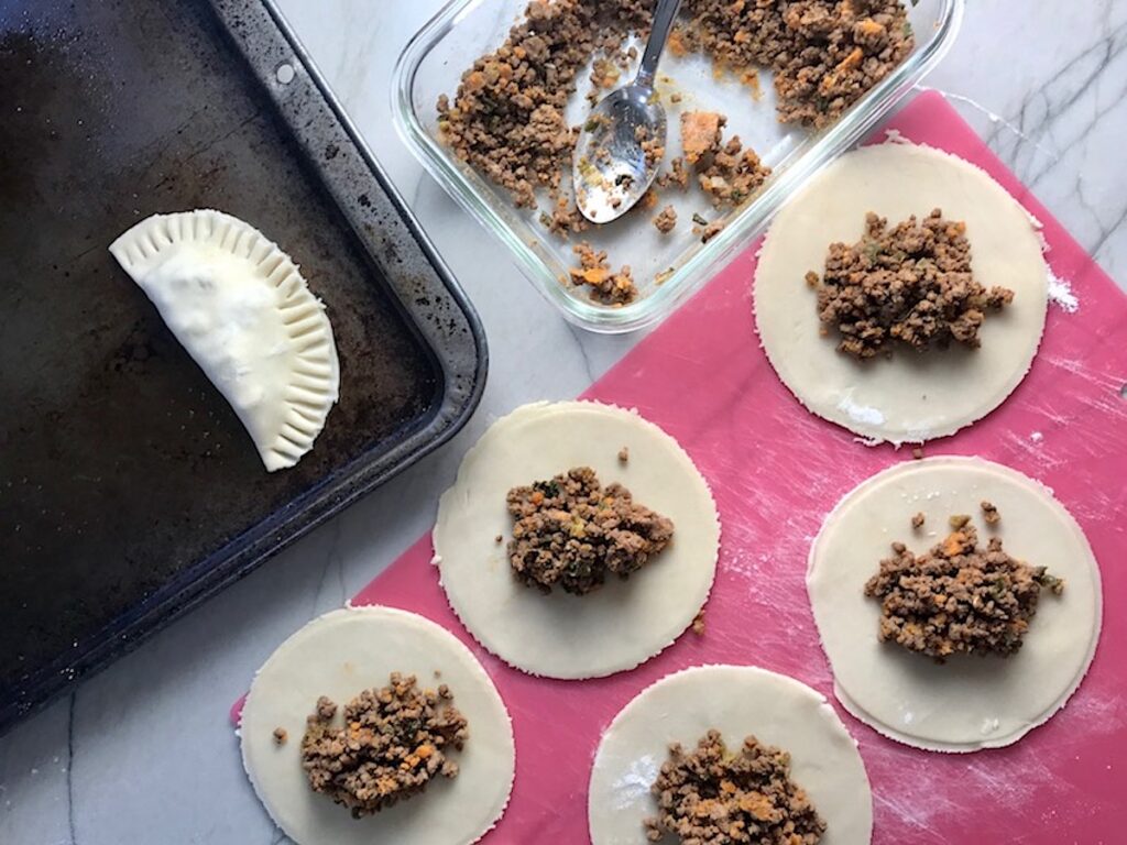 Making Ground Spiced Beef Empanadas - crust rounds with filling in center, beef filling in dish, and empanada on a pan. Flaky, buttery pastry on the outside with a savory, smokey, salty ground beef filling.