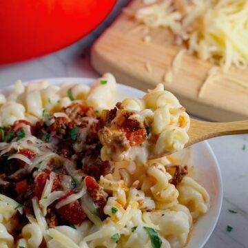 Chili Mac and Cheese on a plate with fork. This Recipe has creamy and cheesy pasta topped with smokey, tangy, savory beef chili! #macandcheese #chilirecipes