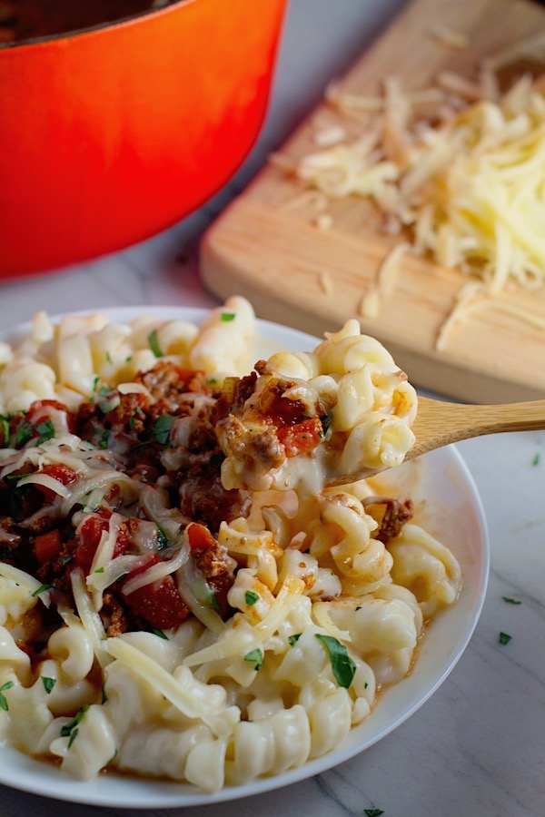 Chili Mac and Cheese on a plate with fork.  This Recipe has creamy and cheesy pasta topped with smokey, tangy, savory beef chili! #macandcheese #chilirecipes