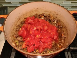 Diced tomatoes and beef in pot for Chili Mac and Cheese. This Recipe has creamy and cheesy pasta topped with smokey, tangy, savory beef chili! #macandcheese #chilirecipes