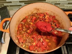 Adding tomato paste to chili pot for Chili Mac and Cheese. This Recipe has creamy and cheesy pasta topped with smokey, tangy, savory beef chili! #macandcheese #chilirecipes