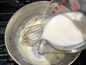 Adding slurry to roux for Chili Mac and Cheese. This Recipe has creamy and cheesy pasta topped with smokey, tangy, savory beef chili! #macandcheese #chilirecipes
