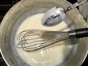 sauce with whisk and spoon for Chili Mac and Cheese. This Recipe has creamy and cheesy pasta topped with smokey, tangy, savory beef chili! #macandcheese #chilirecipes