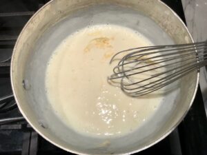 Whisking cheese sauce for Chili Mac and Cheese. This Recipe has creamy and cheesy pasta topped with smokey, tangy, savory beef chili! #macandcheese #chilirecipes