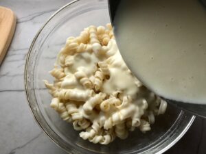 Pouring Cheese sauce over pasta for Chili Mac and Cheese. This Recipe has creamy and cheesy pasta topped with smokey, tangy, savory beef chili! #macandcheese #chilirecipes