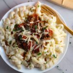 Chili Mac and Cheese on a plate with fork. This Recipe has creamy and cheesy pasta topped with smokey, tangy, savory beef chili! #macandcheese #chilirecipes
