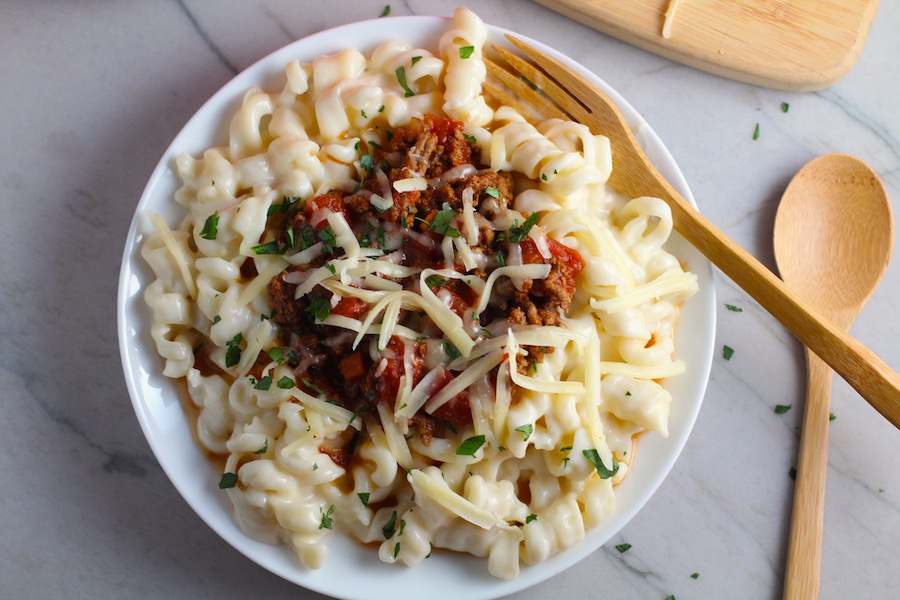 Chili Mac and Cheese on a plate with fork. This Recipe has creamy and cheesy pasta topped with smokey, tangy, savory beef chili! #macandcheese #chilirecipes