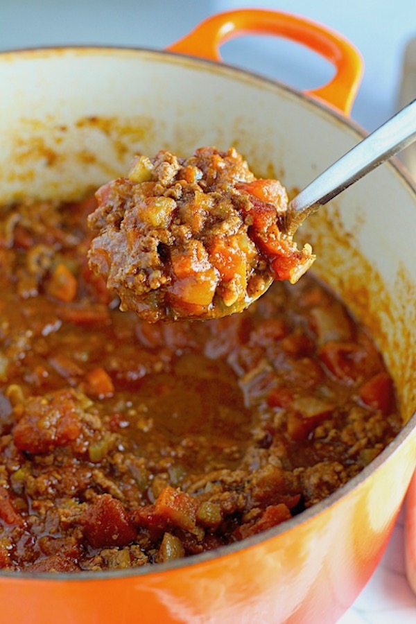 Scooping Chili out of pot for Chili Mac and Cheese. This Recipe has creamy and cheesy pasta topped with smokey, tangy, savory beef chili! #macandcheese #chilirecipes