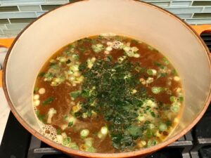 Cilantro added to broth for Creamy Chicken Green Enchilada Soup. It's creamy, hearty, slightly spicy with green chiles and smokey seasonings that bring so much depth. Corn tortilla strips act like the noodles in this soup!