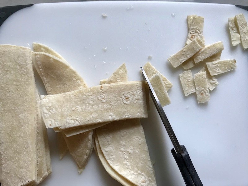 Cutting corn tortillas for Creamy Chicken Enchilada Soup. It's creamy, hearty, slightly spicy with green chiles and smokey seasonings that bring so much depth. Corn tortilla strips act like the noodles in this soup!