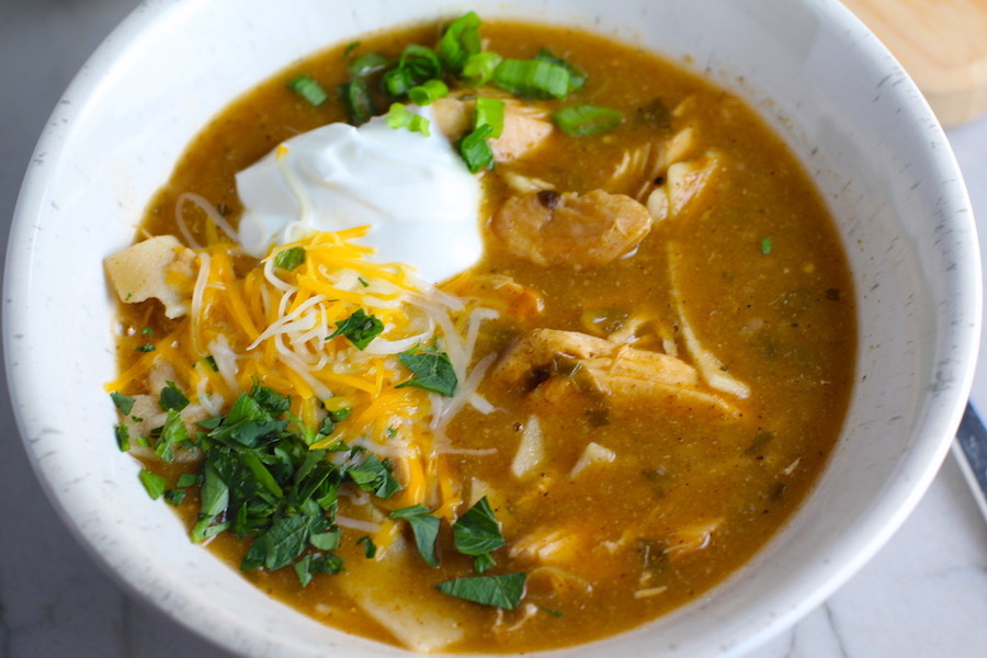 Creamy Chicken Enchilada Soup in a bowl topped with cheese, sour cream, and cilantro! It's creamy, hearty, slightly spicy with green chiles and smokey seasonings that bring so much depth. Corn tortilla strips act like the noodles in this soup!