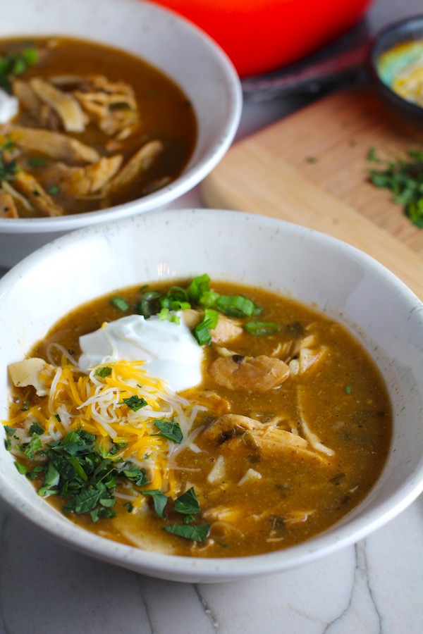Creamy Chicken Enchilada Soup in a bowl topped with cheese, sour cream, and cilantro! It's creamy, hearty, slightly spicy with green chiles and smokey seasonings that bring so much depth. Corn tortilla strips act like the noodles in this soup!