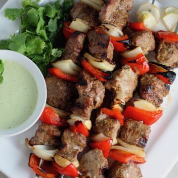 Garlic Steak Kabobs with red pepper and onion on platter with a Creamy Cilantro Sauce! #beefkabobs #steakkabobs