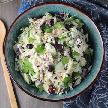 Greek Lemon Orzo Salad with Kalamata Olives, Cucumbers, and Feta Cheese in a bowl with wood spoon! It's combined with a creamy lemon dressing that's bright and light!