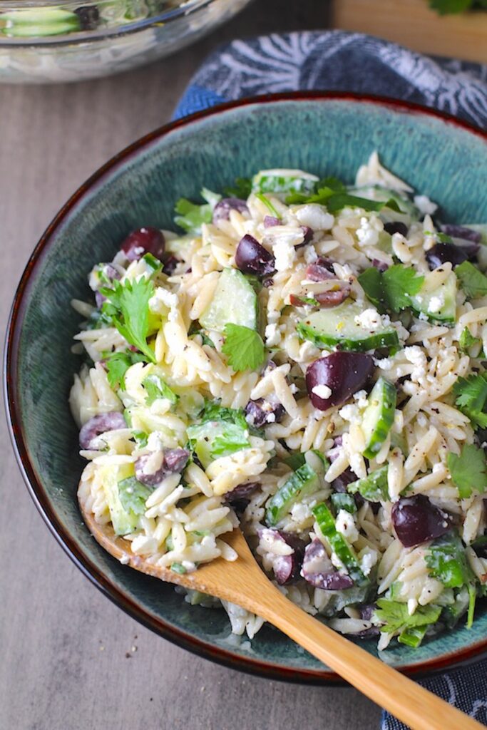 Greek Lemon Orzo Salad with Kalamata Olives, Cucumbers, and Feta Cheese in a bowl with lemon on side. It's mixed with a creamy lemon dressing that's bright and light!