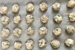 Raw Ground Chicken Greek Meatballs on a pan. These meatballs have garlic, feta, parsley, and oregano