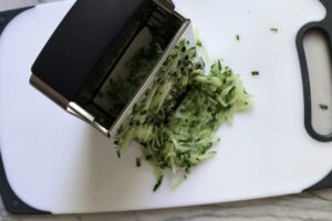 Grating cucumber for Tzatziki sauce to go with Chicken Greek Meatballs. These meatballs have garlic, feta, parsley, and oregano.