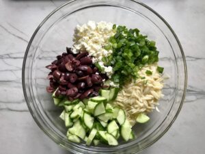 Cucumber, Kalamata Olives, Feta Cheese, Scallions, and orzo all separate in bowl for Greek Orzo Salad.