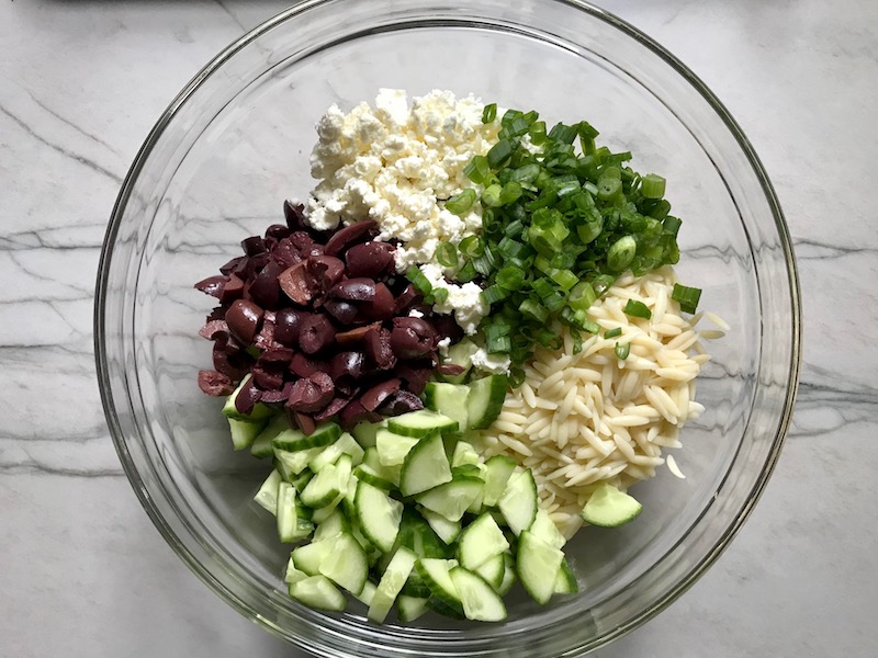 Cucumber, Kalamata Olives, Feta Cheese, Scallions, and orzo all separate in bowl for Greek Orzo Salad.