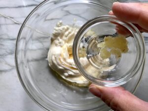 Adding minced garlic to Lemon dressing for Greek Orzo Salad with Kalamata Olives, Cucumbers, and Feta Cheese.
