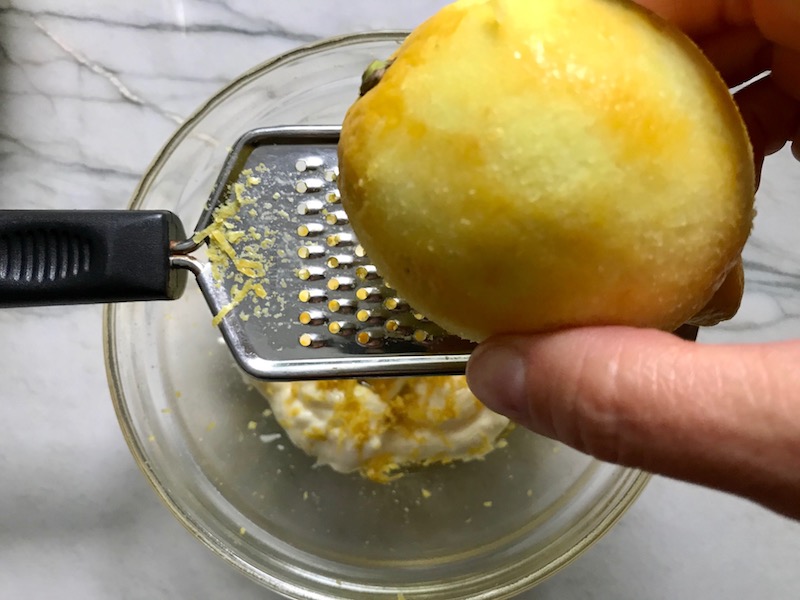 Zesting Lemon over bowl for Greek Orzo Salad with Kalamata Olives, Cucumbers, and Feta Cheese.
