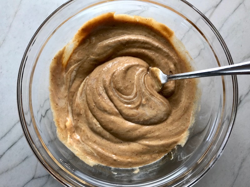 BBQ sauce mixed with sour cream in a bowl with a spoon on counter for a BBQ Chicken Pizza Recipe