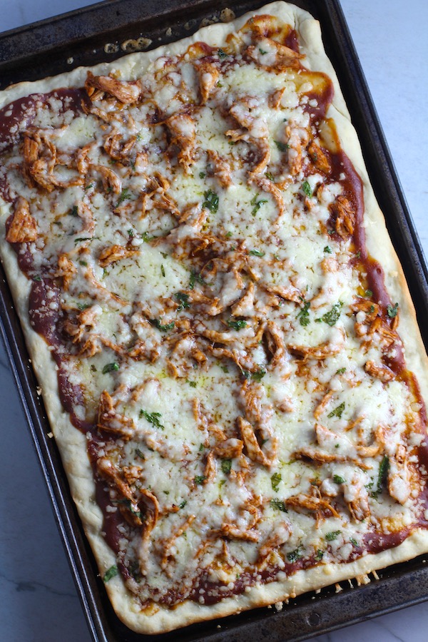 Whole BBQ Chicken Pizza in a rectangle sheet pan with homemade pizza crust, tangy and creamy BBQ sauce, hearty shredded chicken, cheddar cheese and coleslaw on top!