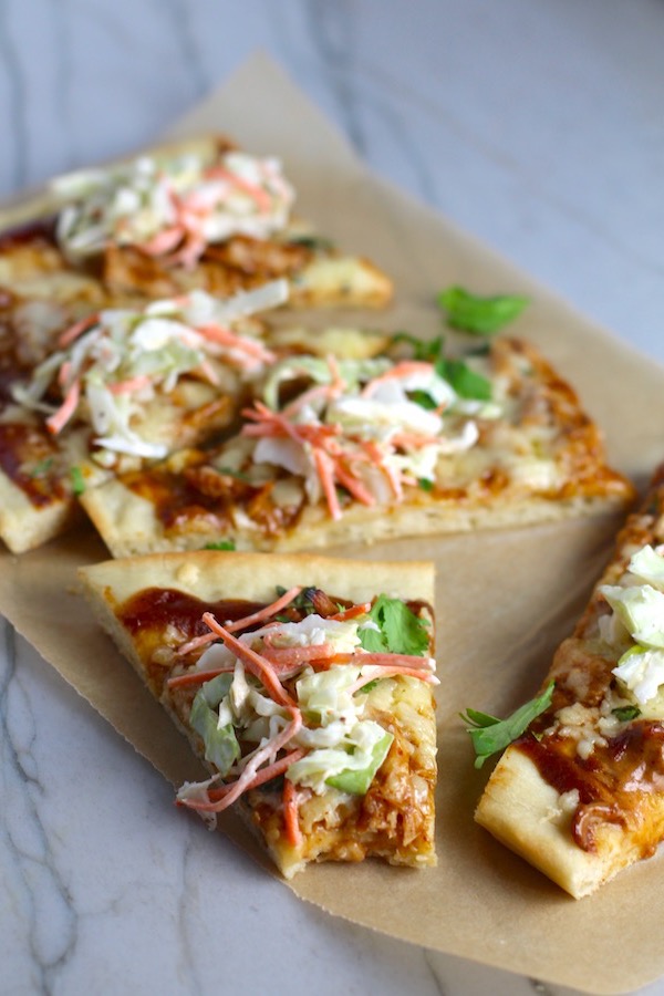 Sliced BBQ Chicken Pizza recipe with coleslaw and cilantro on top. It has homemade pizza crust, tangy and creamy BBQ sauce, hearty shredded chicken, cheddar cheese and coleslaw on top!