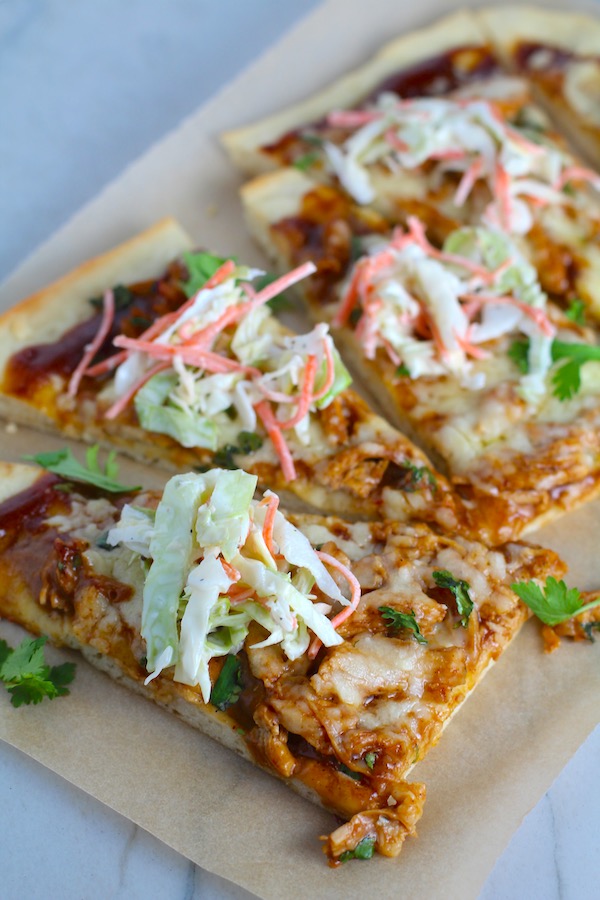 Sliced BBQ Chicken Pizza with coleslaw and cilantro on top. It has homemade pizza crust, tangy and creamy BBQ sauce, hearty shredded chicken, cheddar cheese and coleslaw on top!