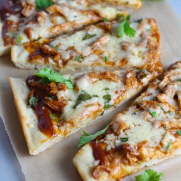 Sliced BBQ Chicken Pizza Recipe with cilantro on top. It has homemade pizza crust, tangy and creamy BBQ sauce, hearty shredded chicken, cheddar cheese and coleslaw on top!