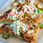 Sliced BBQ Chicken Pizza recipe with coleslaw and cilantro on top. It has homemade pizza crust, tangy and creamy BBQ sauce, hearty shredded chicken, cheddar cheese and coleslaw on top!   