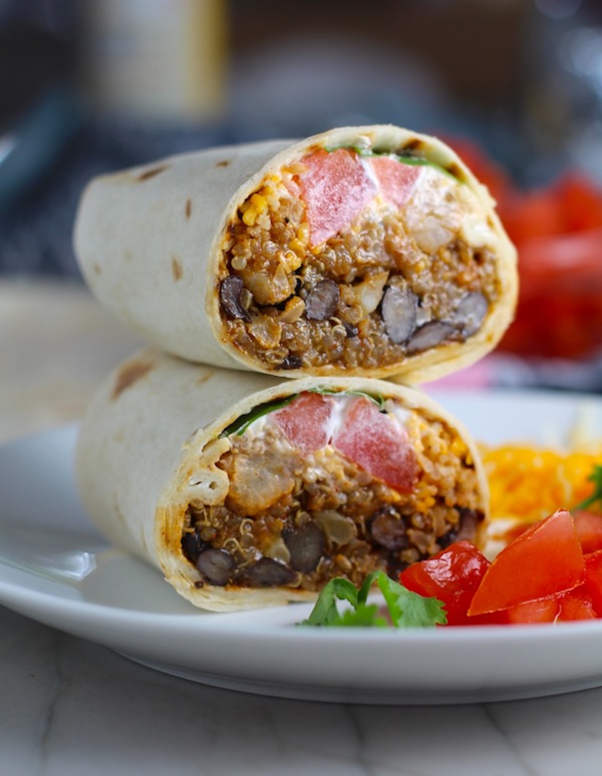 Burritos with Black Beans and Quinoa recipe cut in half and stacked on plate. Packed with protein and fiber, but also cheese, tomato, cilantro, and sour cream! The vegetarian 'meat' is taco-seasoned quinoa, black beans, and cauliflower.