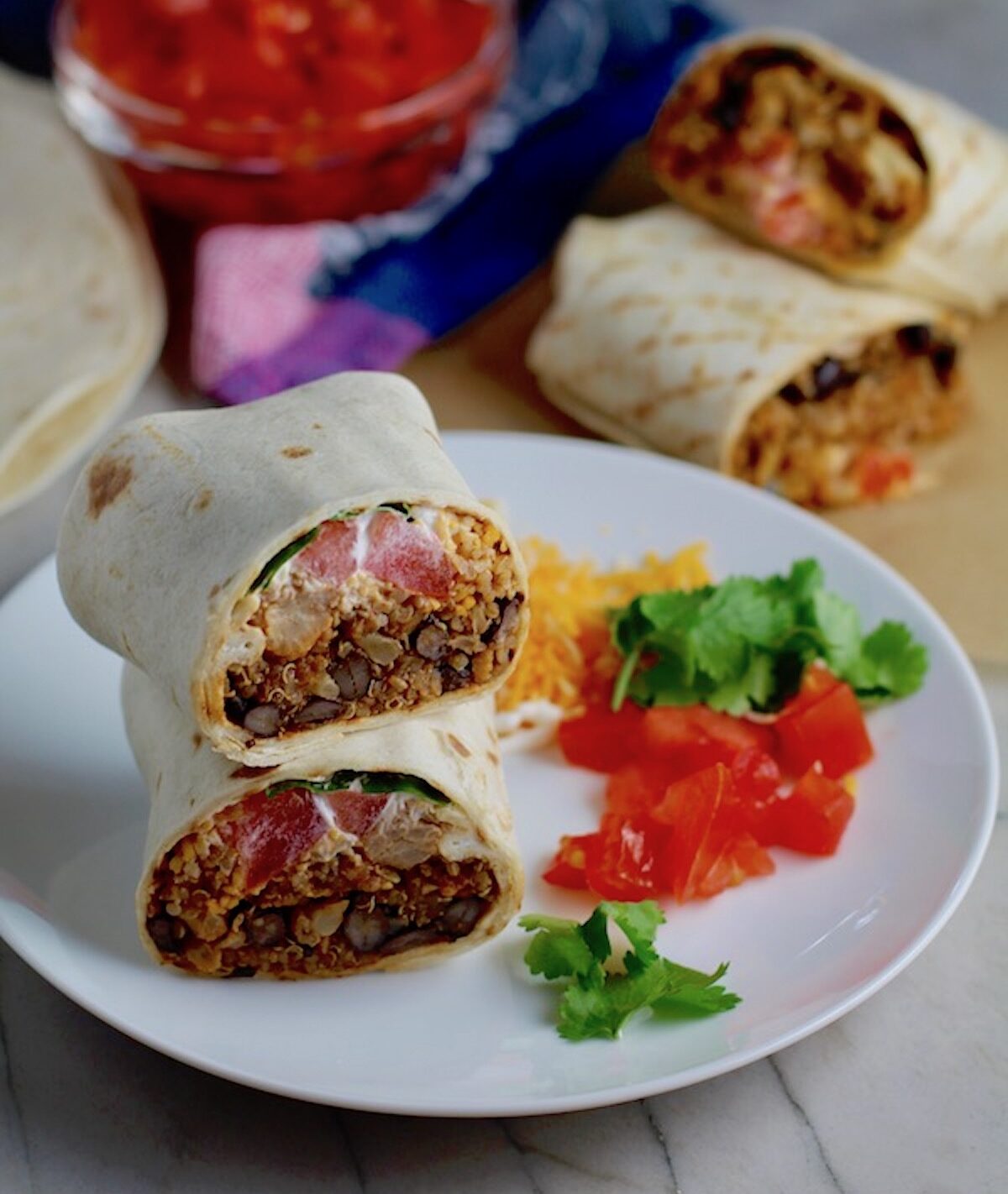 Burritos with Black Beans and Quinoa recipe cut in half and stacked on plate. Packed with protein and fiber, but also cheese, tomato, cilantro, and sour cream! The vegetarian 'meat' is taco-seasoned quinoa, black beans, and cauliflower.