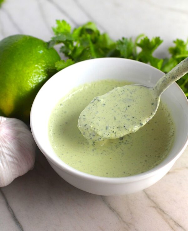 Cilantro Cream sauce in bowl with spoon for Garlic Steak Kabobs. Lime, garlic, and cilantro on counter. #beefkabobs #steakkabobs