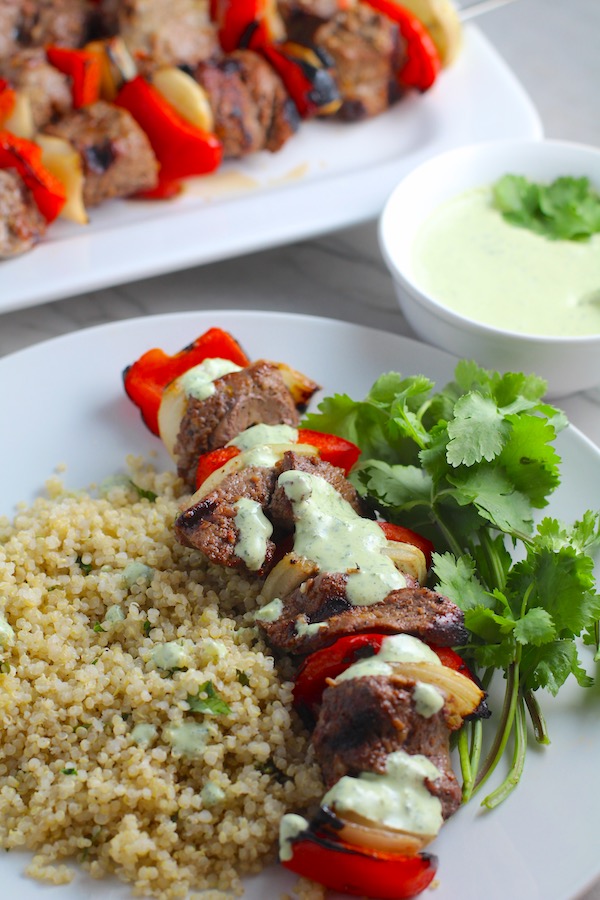 Garlic Steak Kabobs with red pepper and onion on plate with quinoa. Creamy Cilantro Sauce drizzled on top! #beefkabobs #steakkabobs