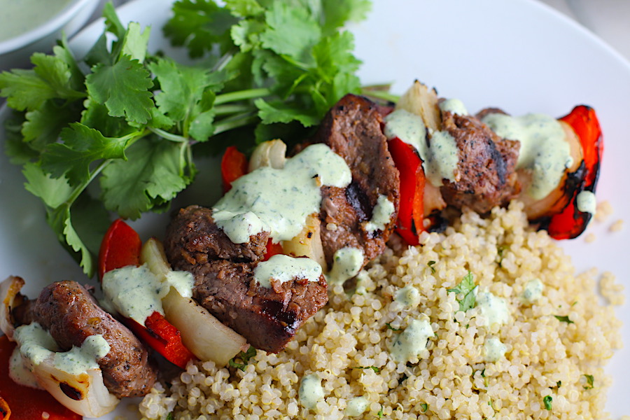 Garlic Steak Kabobs with red pepper and onion on plate with quinoa. Creamy Cilantro Sauce drizzled on top! #beefkabobs #steakkabobs