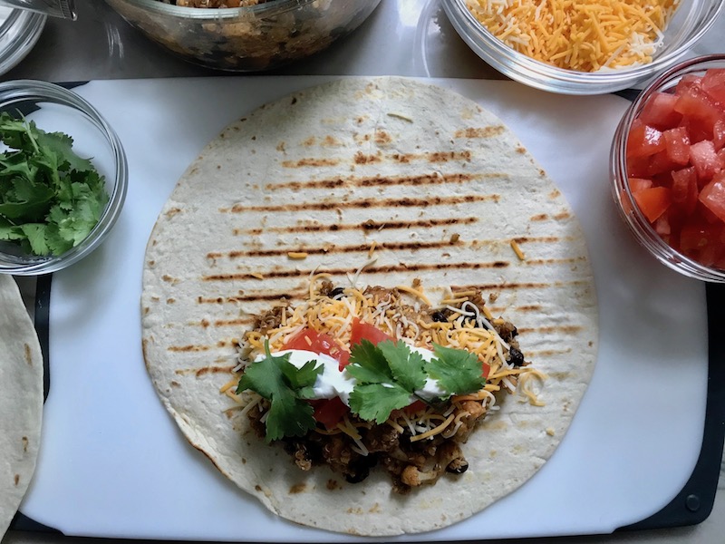 Tortilla with Quinoa Black Bean filling, cheese, and tomatoes. These Burritos are packed with protein and fiber, but also cheese, tomato, cilantro, and sour cream! The vegetarian 'meat' is taco-seasoned quinoa, black beans, and cauliflower.