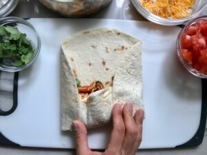 Hand rolling Quinoa Black Bean Burrito. Packed with protein and fiber, but also cheese, tomato, cilantro, and sour cream! The vegetarian 'meat' is taco-seasoned quinoa, black beans, and cauliflower.