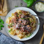 Crockpot Shredded Beef Ragu Recipe with Pappardelle with a fork on plate with parsley, basil, parmesan, and bread on the table. It's so easy to make and has a thick meaty texture and a super rich delicious flavor.