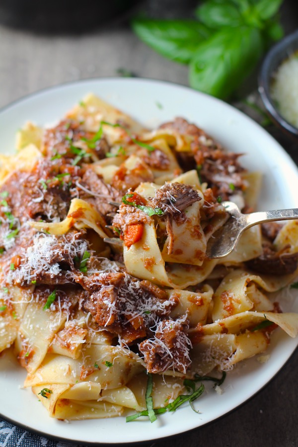 Shredded Beef Ragu Recipe with Pappardelle with a fork on plate with basil and parmesan on the table. It's so easy to make and has a thick meaty texture and a super rich delicious flavor.