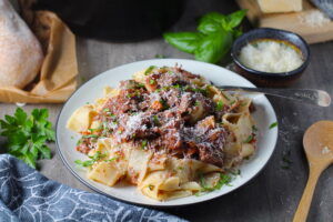 Crockpot Shredded Beef Ragu Recipe with Pappardelle with a fork on plate with parsley, basil, parmesan, and bread on the table. It's so easy to make and has a thick meaty texture and a super rich delicious flavor.